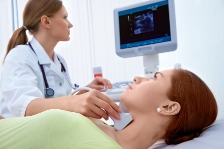 A photo of a woman getting an ultrasound of her thyroid